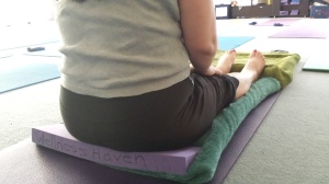 Restorative Seated forward Fold in Staff Pose, with wedge, blankets and cushions for support.