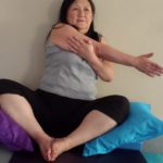 Restorative Sitting Bound Angle Pose with Arm and Shoulder Stretch, with blankets and cushions for support.